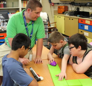 Students using beginning coding to move a purple mouse on a green track.