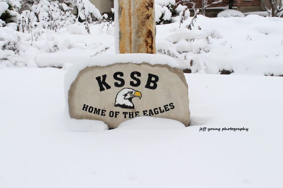 Stone partially covered in snow with eagle head and KSSB Home of the Eagles carved on the front.