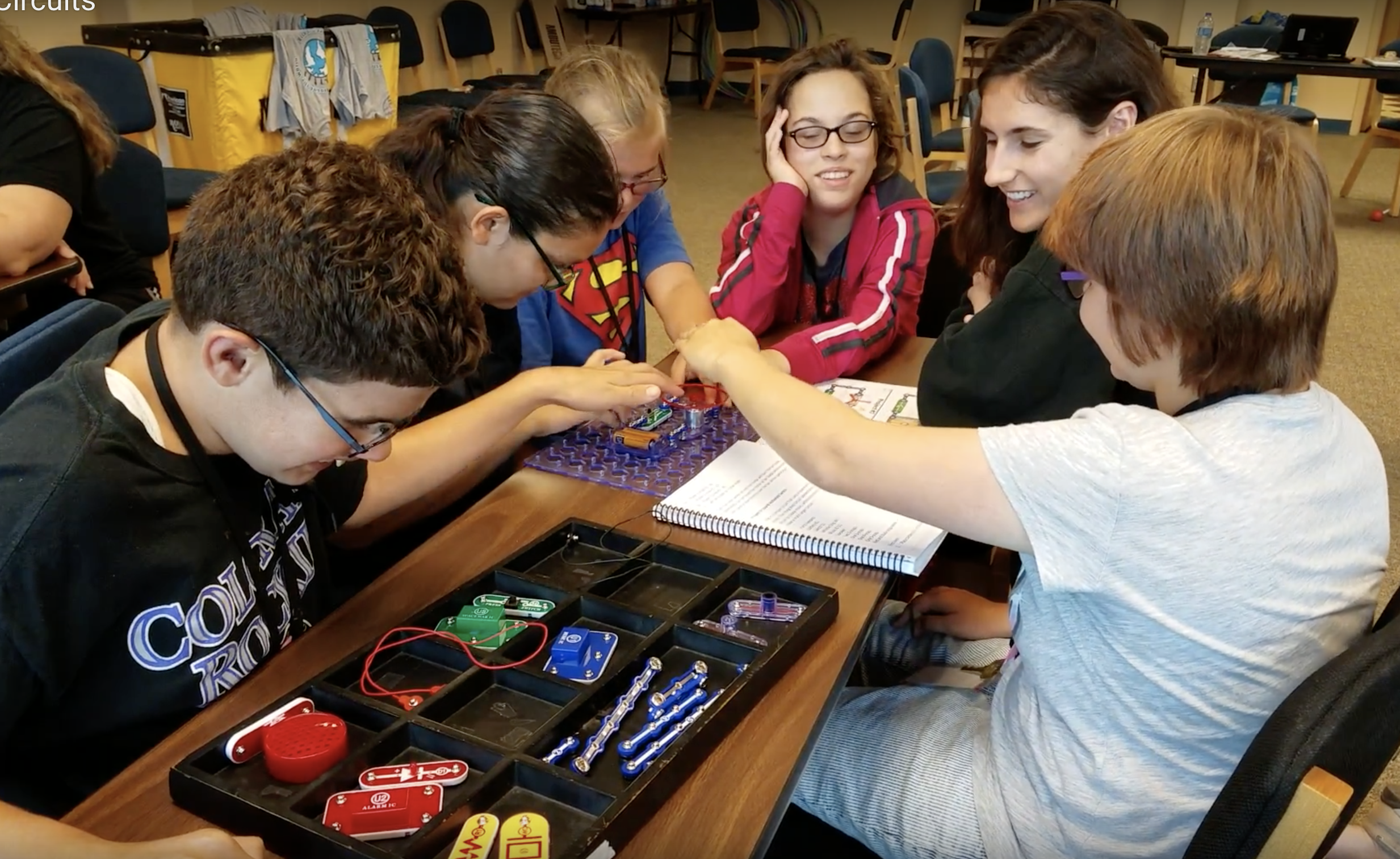 Five students sitting around a table investigating Snap Circuits. A teacher is the facilitator.