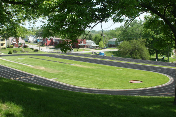 View of Track framed by two large trees to the right and left. The pond and homes are seen in the background.