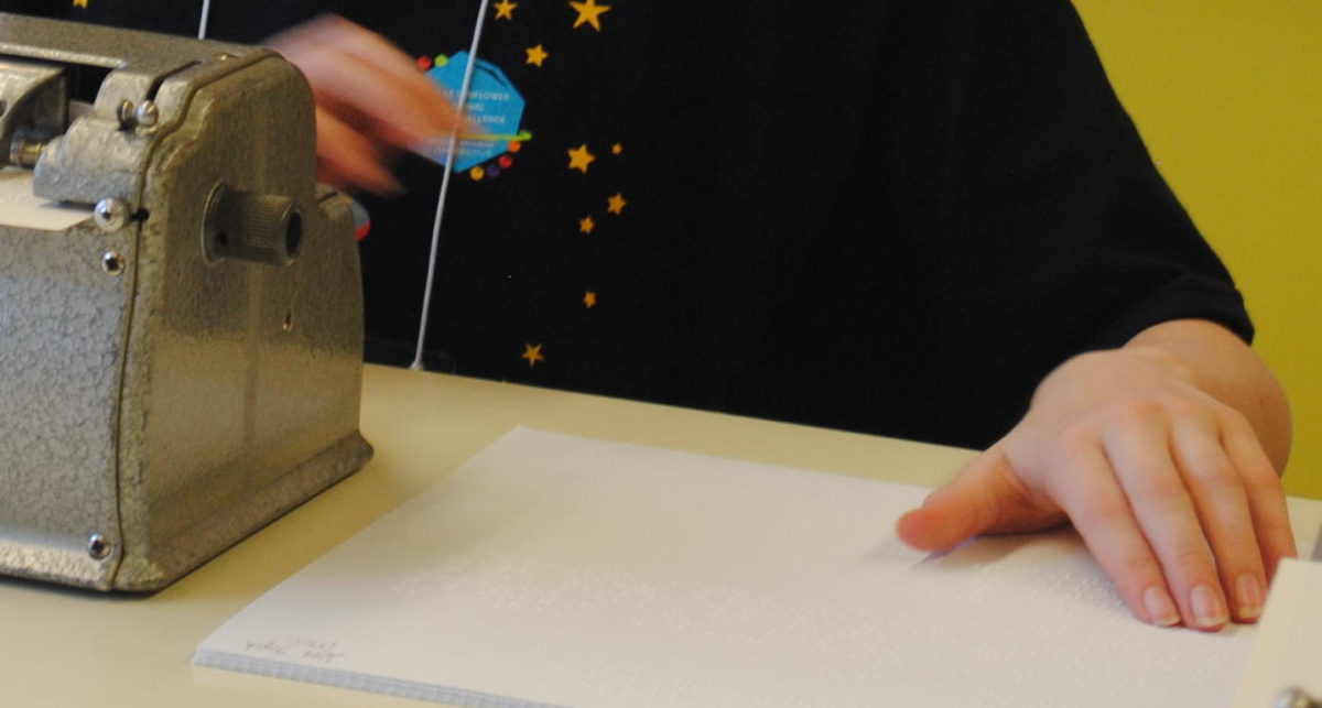 Student with right hand on the brailler and the left hand reading braille.