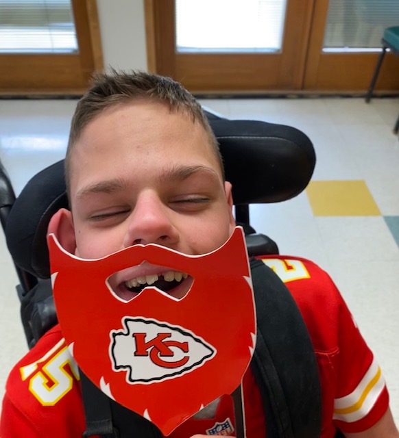 Student holding up a KC Chiefs mask and wearing a KC Chiefs shirt.