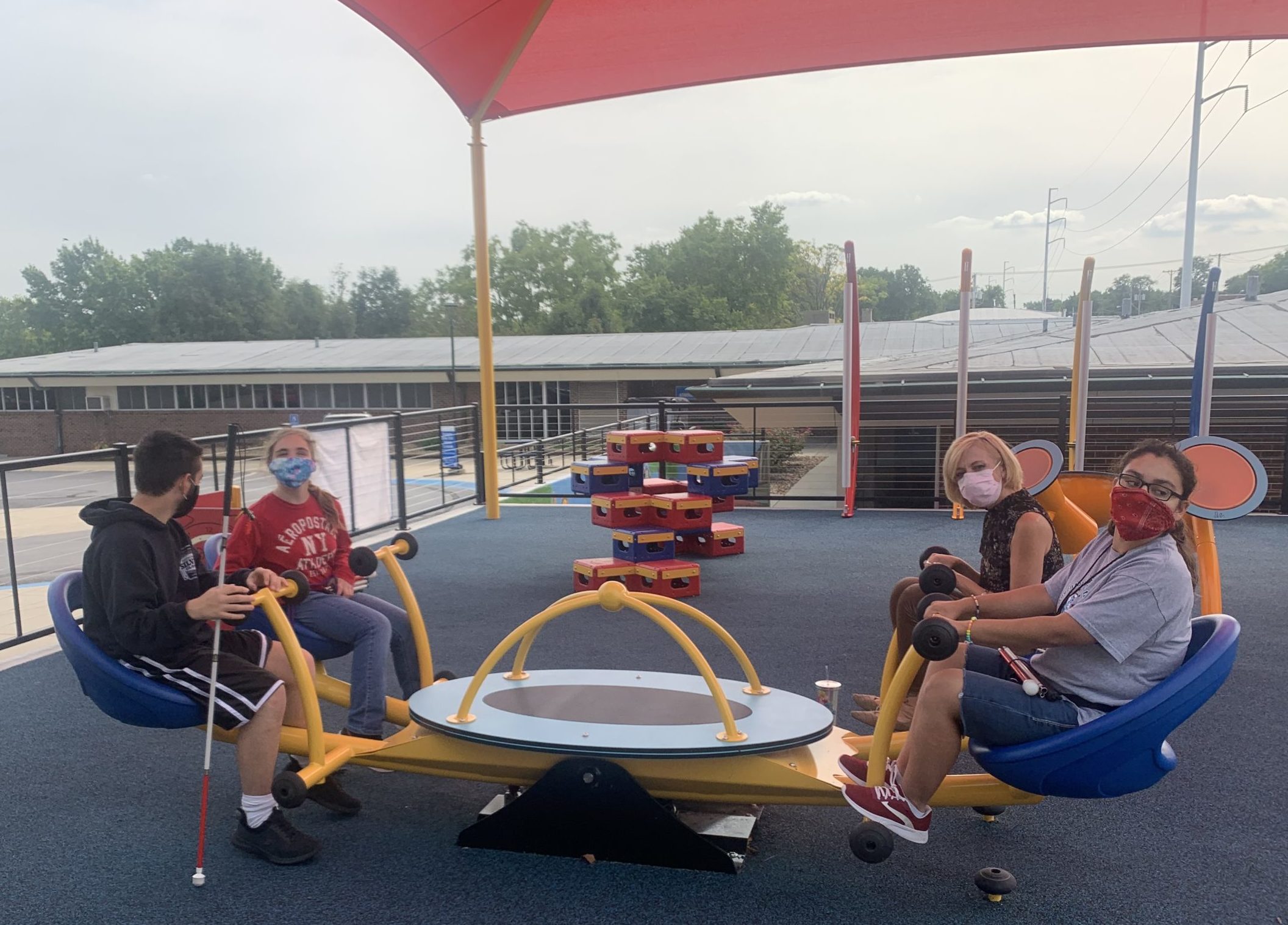 A teacher and three students sitting on the 4 person accessible see saw on the new playground.