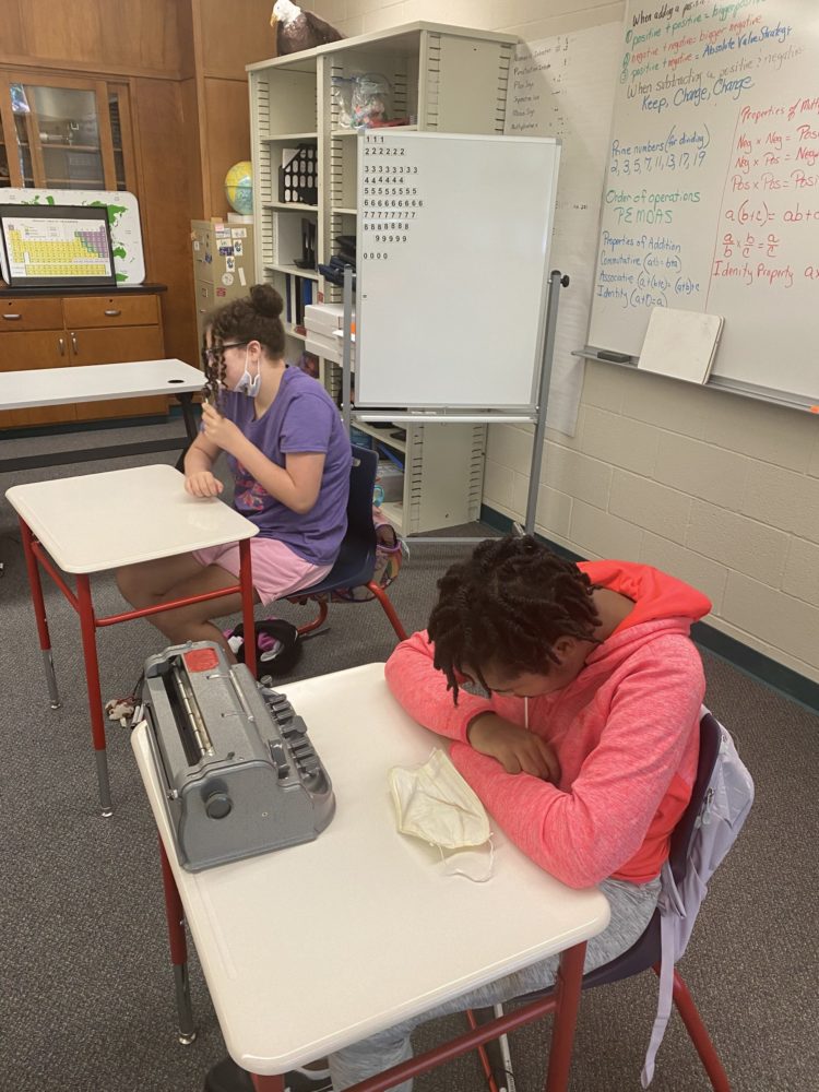 2 students sitting at desks licking tootsie pops