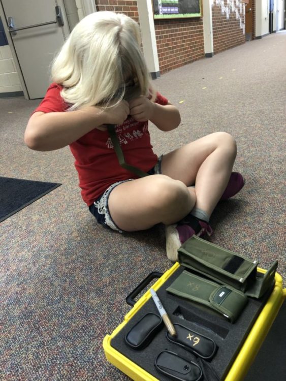 girl with blonde hair and red shirt sitting on the floor looking at different monculars