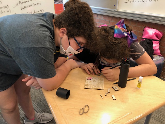 two students leaning over a desk working on a woodworking project