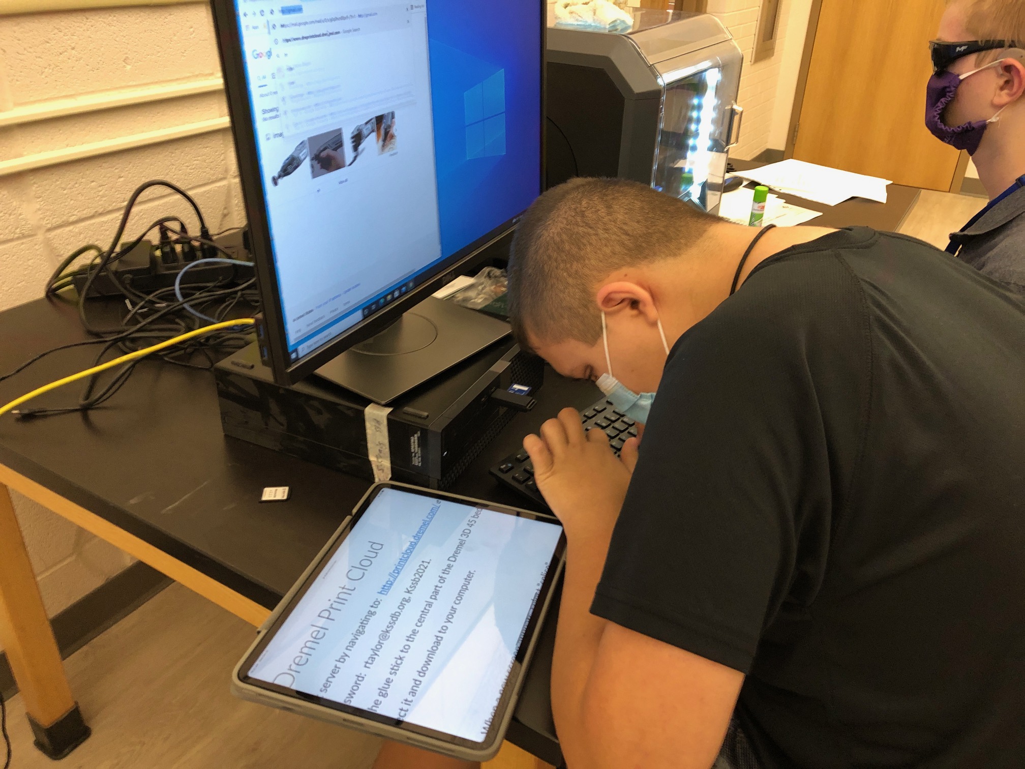 student sitting at a computer typing with directions enlarged on an iPad to his left