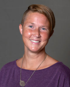 Nicole Drake wearing a dark purple top and a necklace with a leaf.