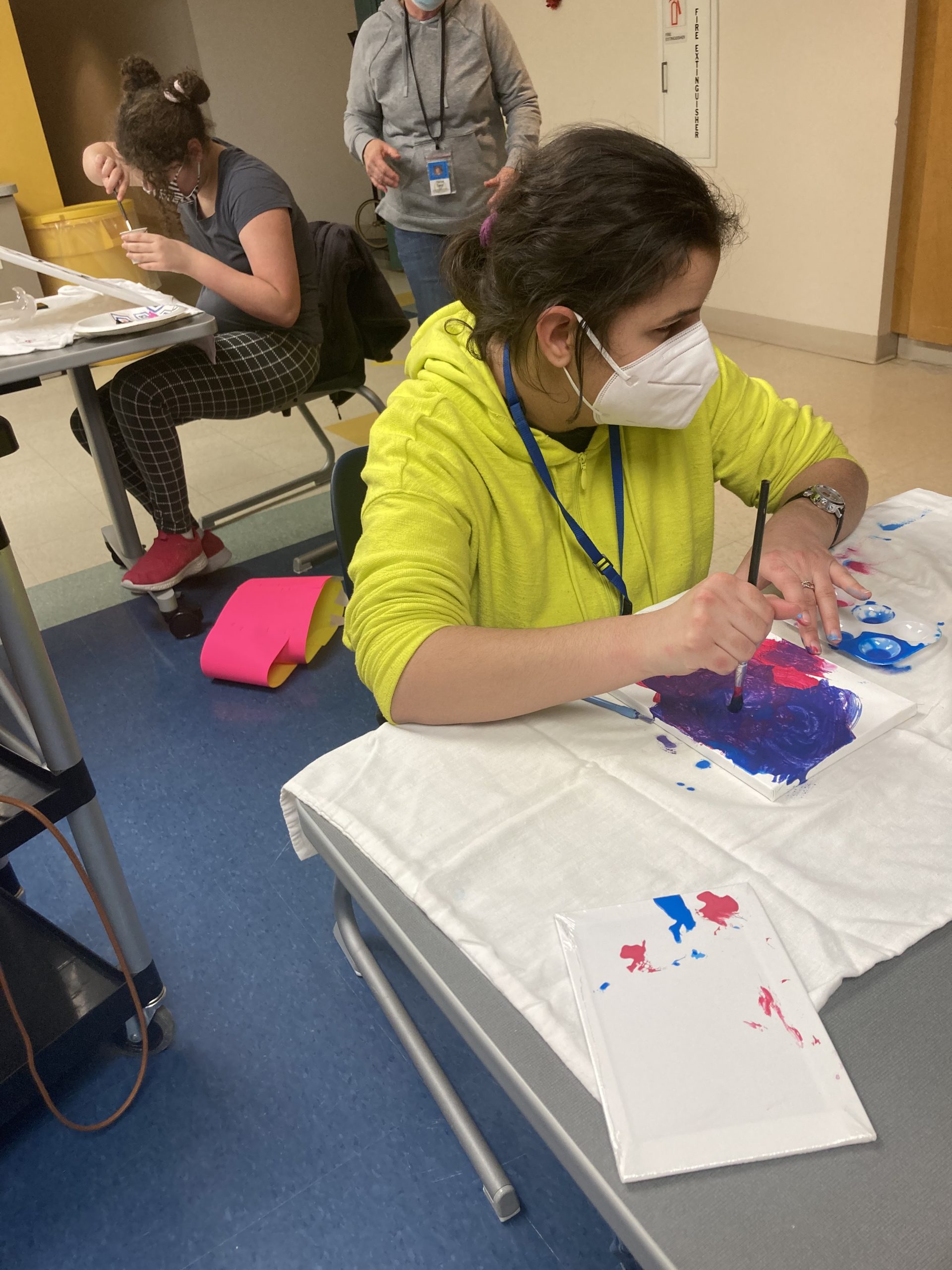 a girl sits at a table and painting on a canvas that lays flat on the table in front of her