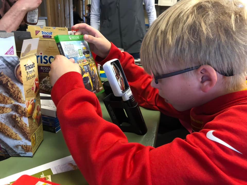 A student uses a magnifier to read a video game case.