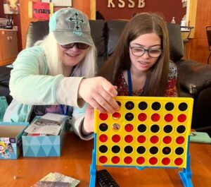 Two smiling girls sit at a table and play Connect 4.