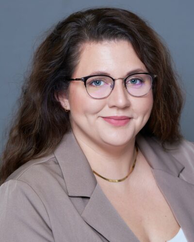 Laura Wohlhuter smiling for the camera with long wavy brown hair and glasses.