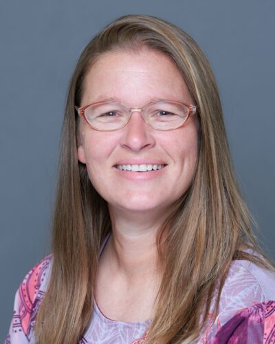 Melissa Schlegel, smiling with long brown hair and glasses