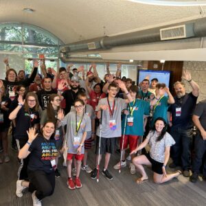A large group of students and adults stand in the Makerspace, smiling wide and celebrating
