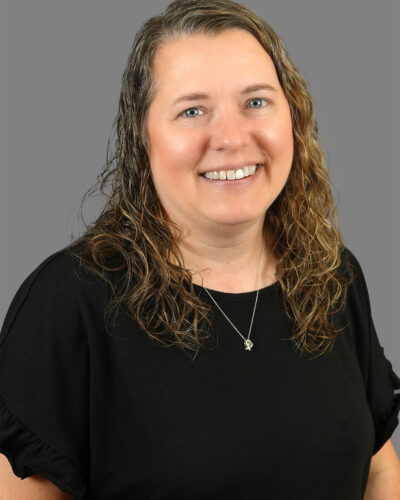 Pam Arbeiter has long, curly brown hair, she wears a black blouse and smiles for the camera.