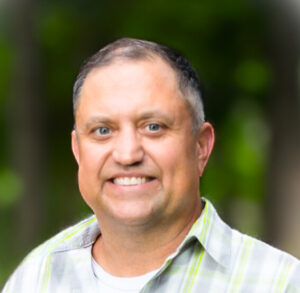 Vince Cianfrone smiles at the camera. He has short gray hair and wears a gray and green plaid shirt.